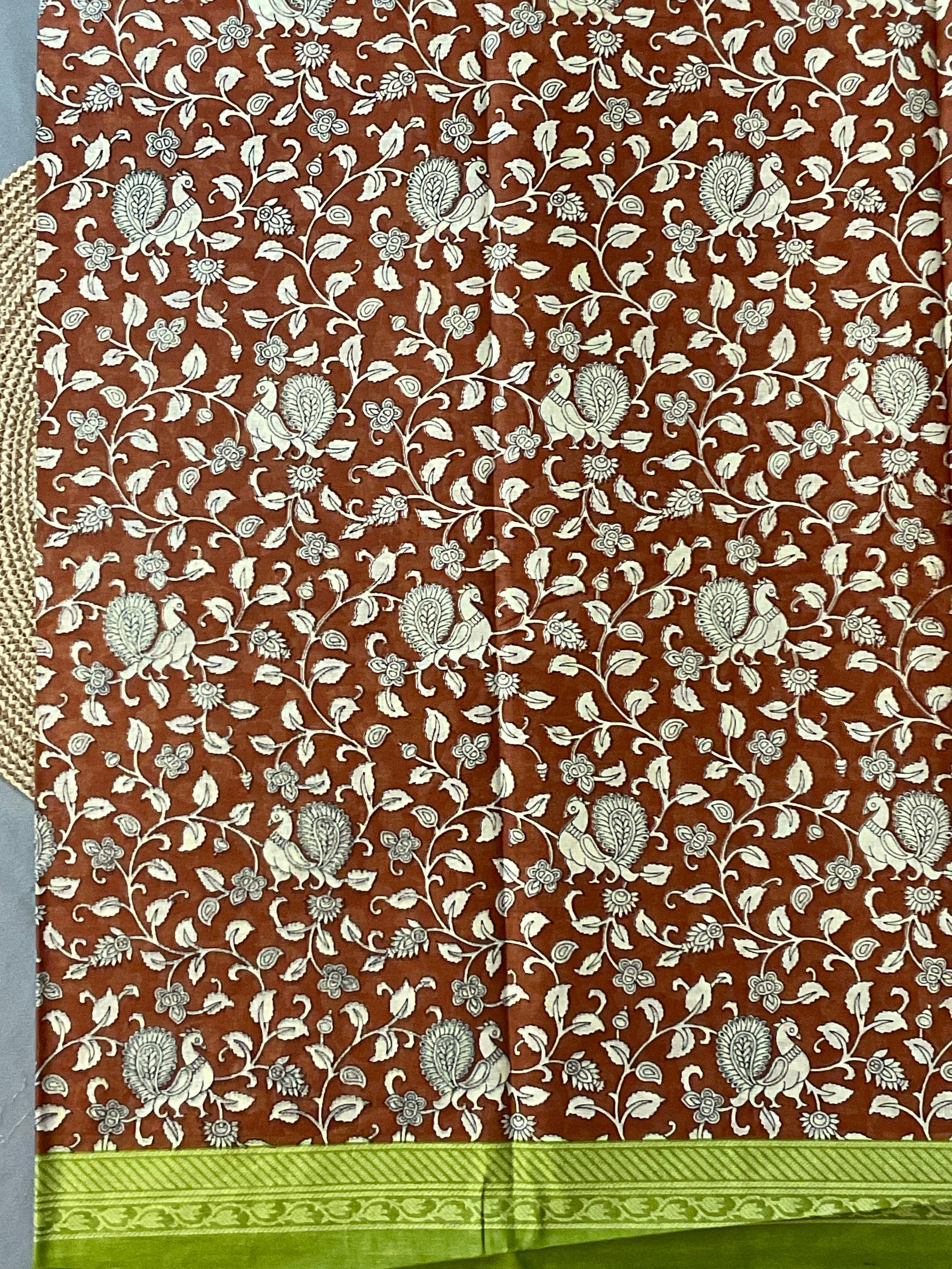 A close-up of a brown fabric with an all-over cream floral and bird pattern, finished with a bright green border along the bottom edge.